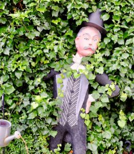 Menschliche Plastik wird von einer Hecke überwuchert.
